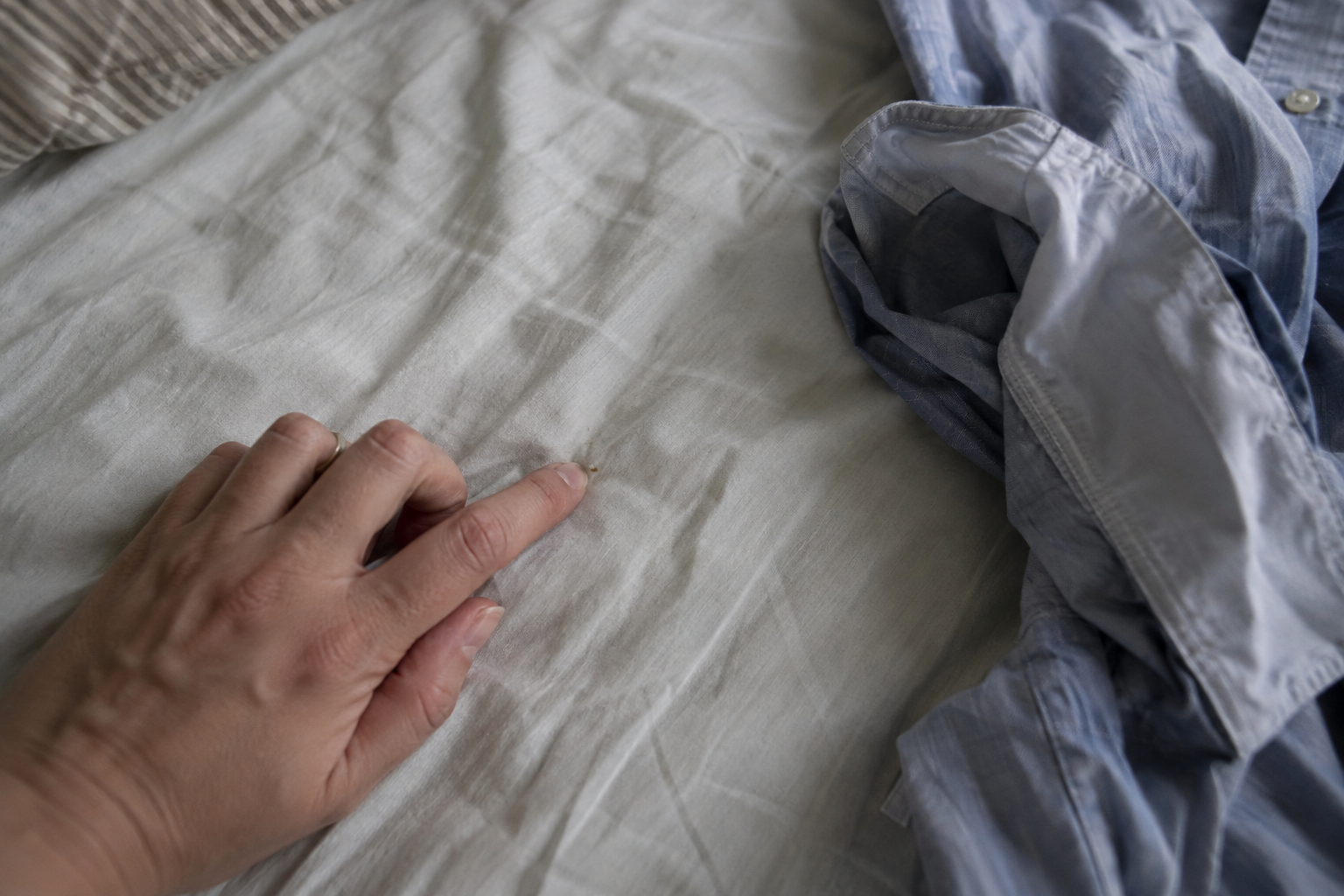 A fingertip picks at a detergent grain in a creased sheet beside an inside-out shirt sleeve.